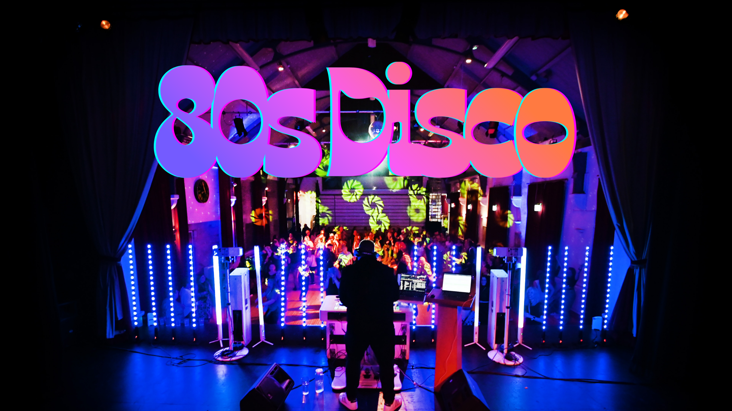Photograph of a nightclub scene featuring a DJ performing in front of a crowd with vibrant blue and purple lighting. Large, colorful "80s Disco" text overlays the top center, highlighting the event's theme and retro atmosphere.